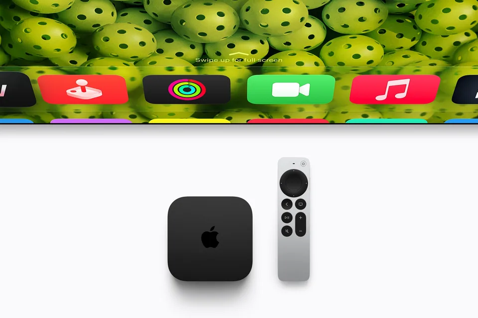Apple TV 4K in Schwarz und silberne Siri Remote unter einem Fernseher mit Startbildschirm