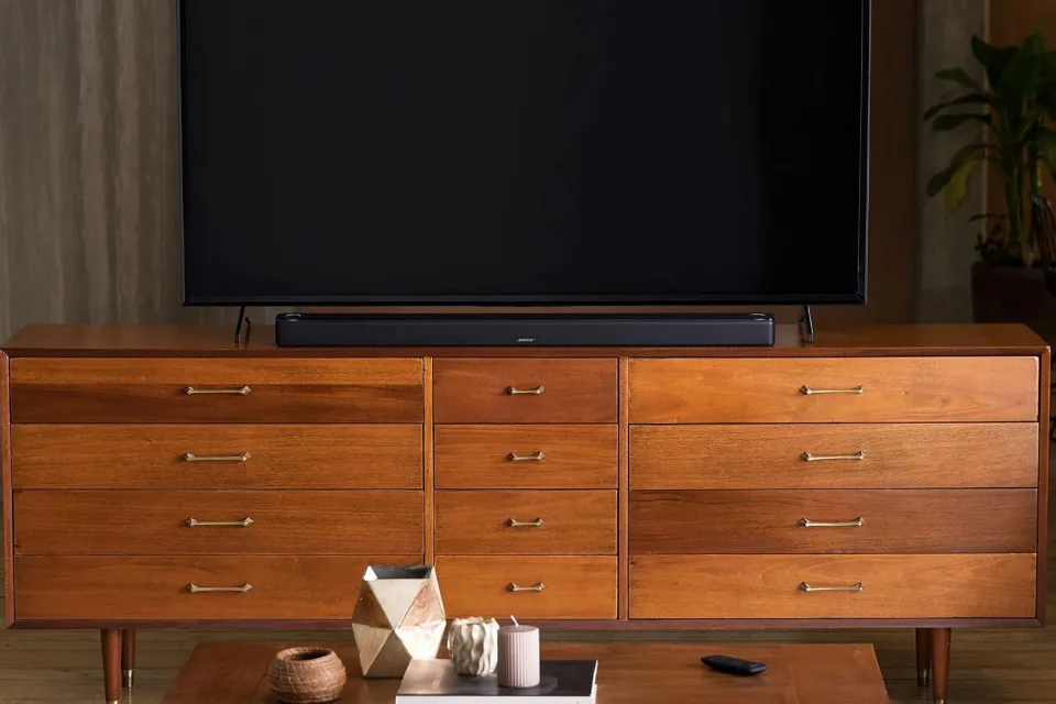 Bose Smart Ultra Soundbar in Schwarz unter einem Fernseher auf einem Holz-Sideboard, Frontansicht