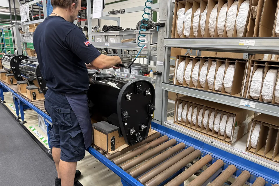 Mitarbeiter montiert ein schwarzes Lautsprechergehäuse auf einem Rollenband