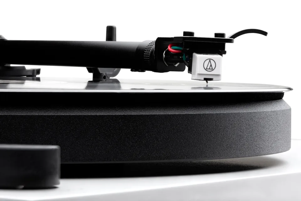 Weißer Audio-Technica-Tonabnehmer an der Headshell eines schwarzen Tonarms über dem Plattenteller