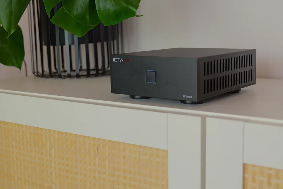 Iotavx B:ound auf einem Metall-Sideboard neben Zimmerpflanze, Glasflasche und Bildschirm