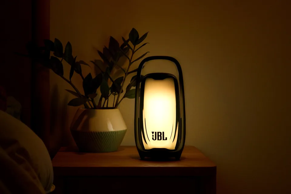 JBL Pulse 6 leuchtet warmweiß als Nachtlicht auf einem Nachttisch neben einer Zimmerpflanze
