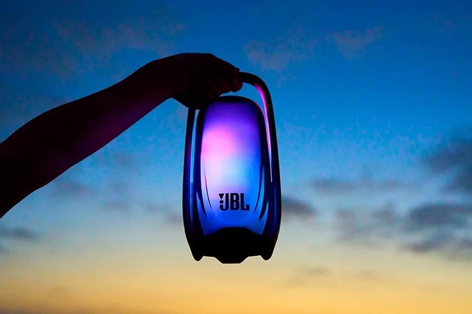 Hand hält den leuchtenden JBL Pulse 6 am Tragegriff vor einem Abendhimmel in die Höhe